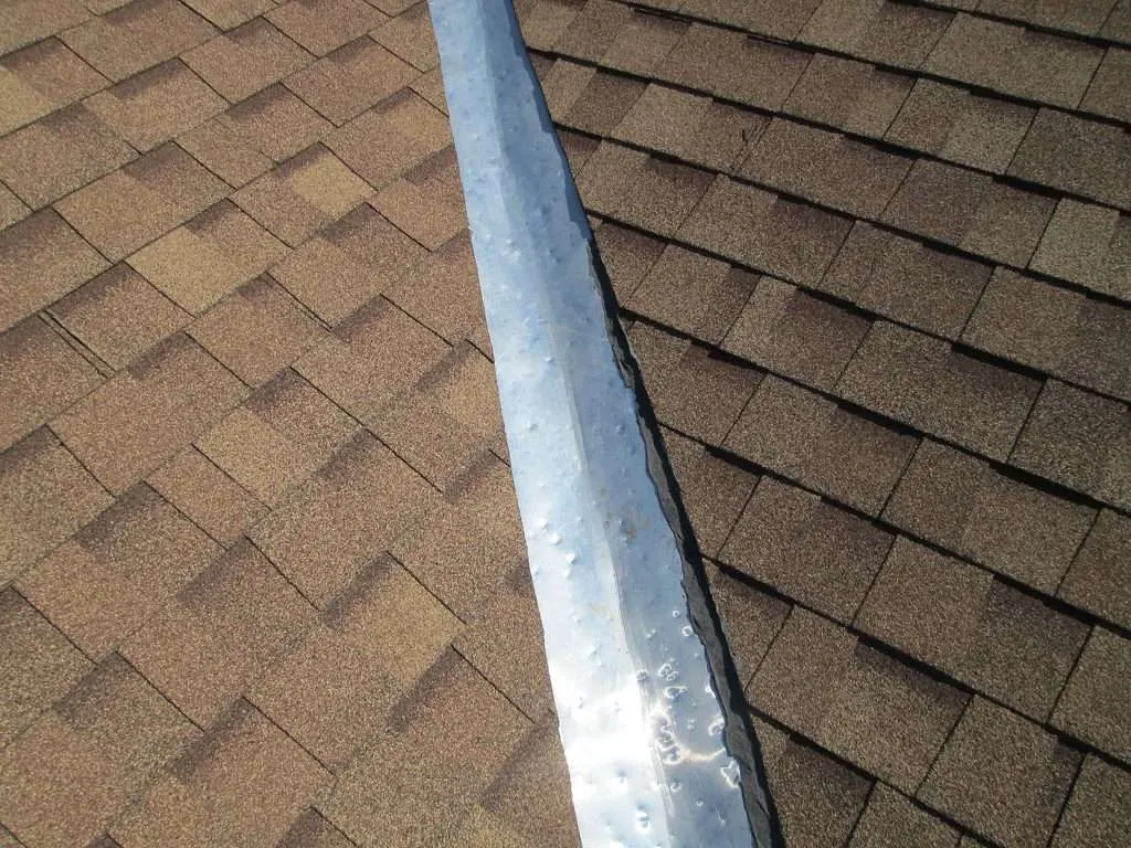 An asphalt roof's metal valley that has visible hail dents.
