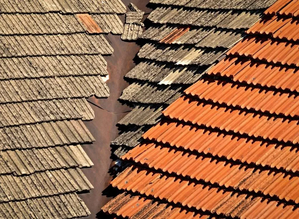 A grey and orange concrete tile roof with broken and chipped tiles.