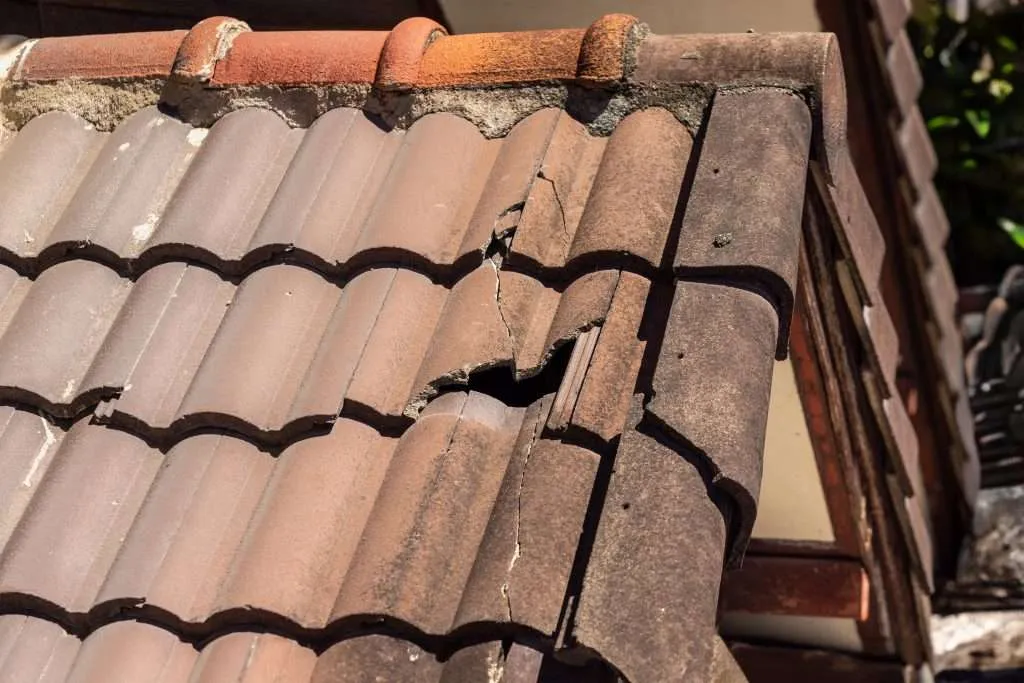 Light colored concrete tiles with radiating cracks and chips from hail damage.