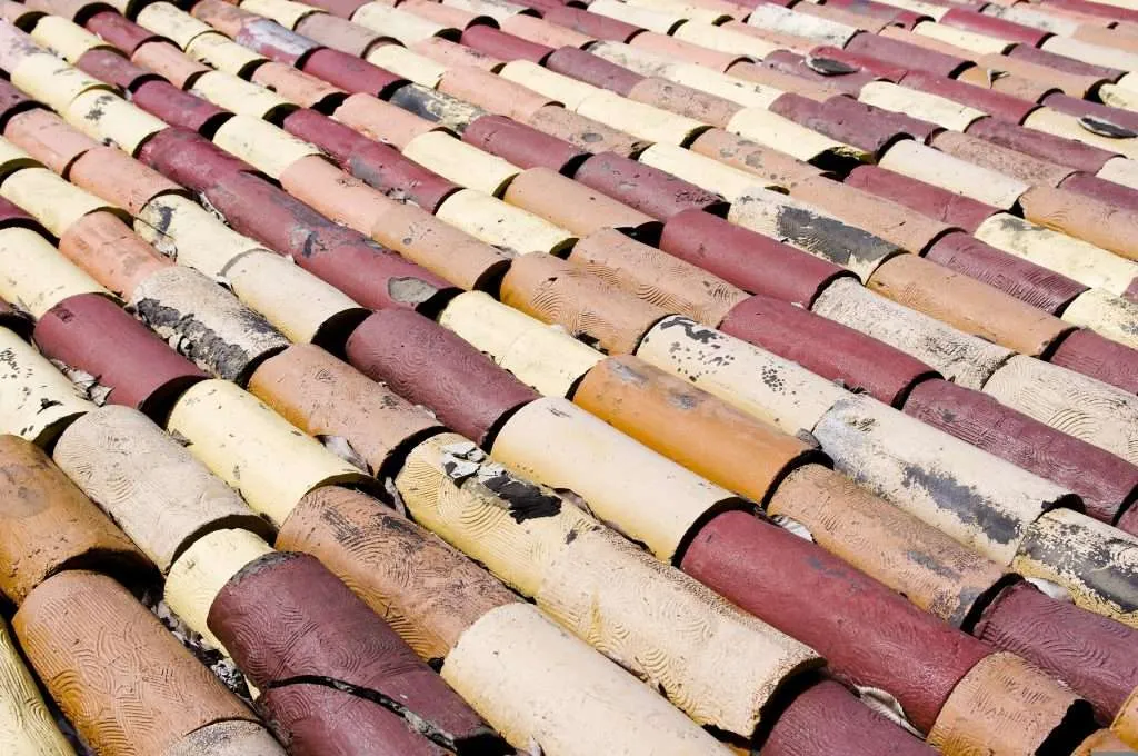 Red, orange, and yellow clay tiles with decorative patterns are chipped, cracked, and broken by hail stones in some places.